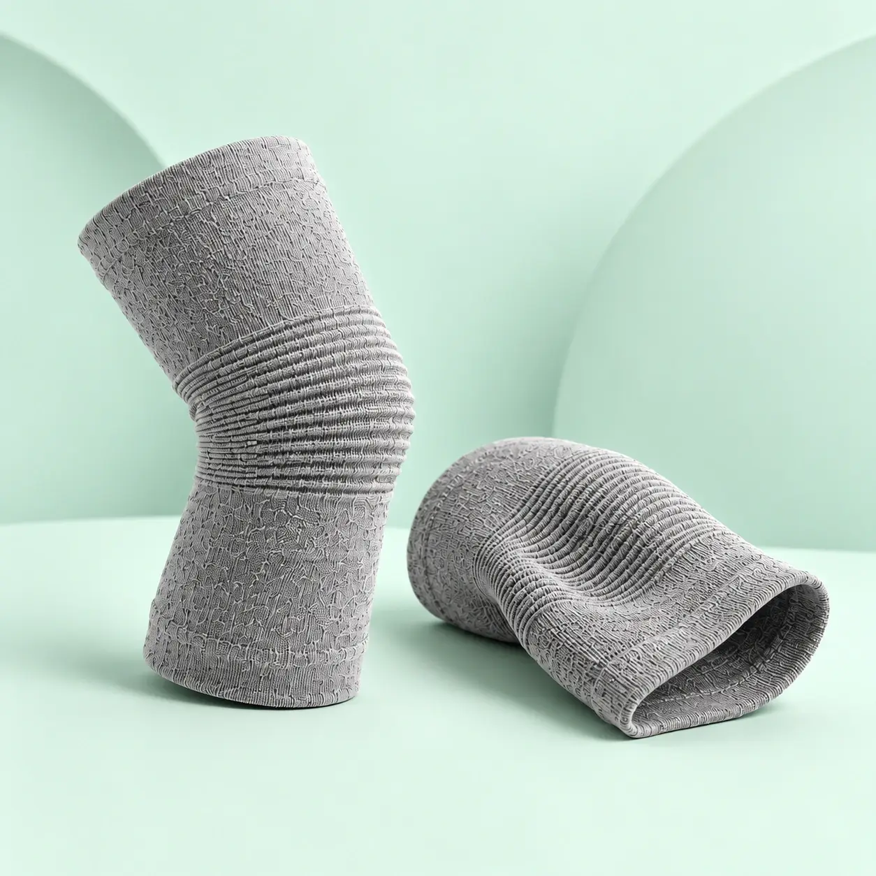 Two gray bamboo knee sleeves on a sculpted mint background